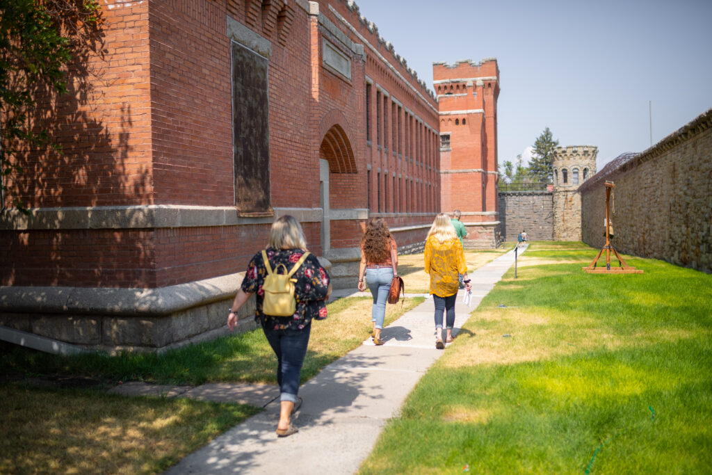 Visitors touring the Old Montana Prison in Deer Lodge, Montana, a historic landmark and museum featuring original 1800s red brick cellblocks, stone walls, and a guard tower open for self-guided and guided tours. Photo by Eric Bunting. 