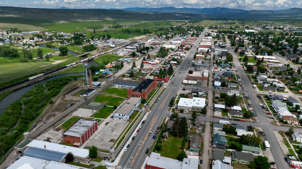 Aerial view of Deer Lodge, Montana, a small historic town in Powell County along I-90, featuring the Old Montana Prison museum, Clark Fork River, and sweeping views of the surrounding valley and mountains. Photo by Sarah Bolt, Tempest Technologies. 