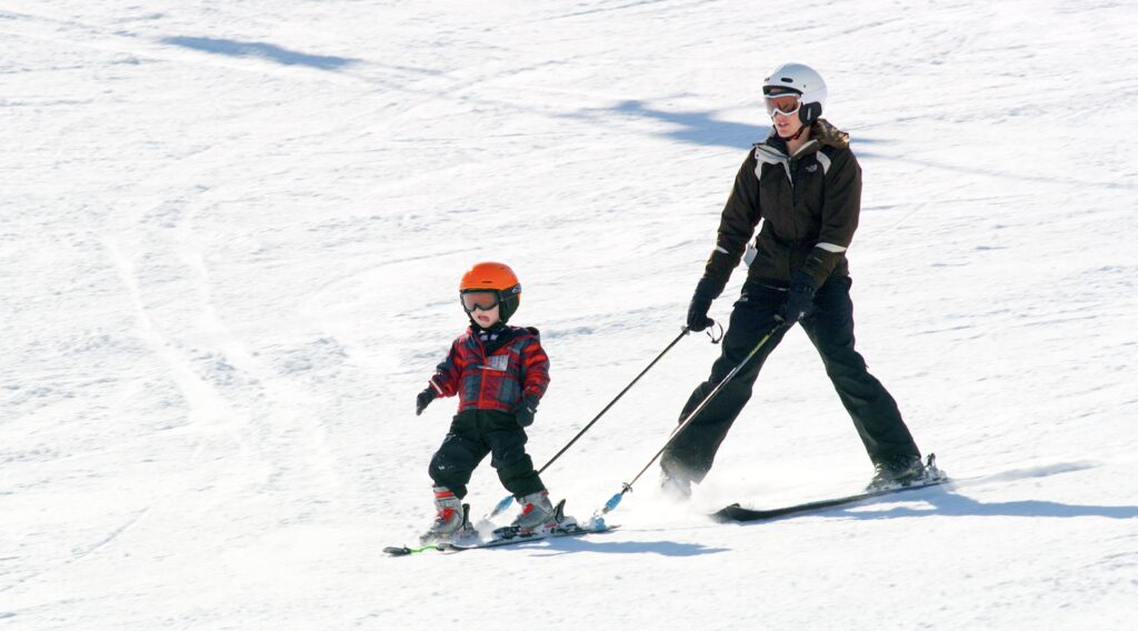 Mother holding tethers to young son skis while he learns to stop and turn on skis and snow at Great Divide Ski Area near Helena, Montana. Ski lessons offered at Great Divide Ski Area and it's an excellent hill for beginners in Southwest Montana. Photo by Tempest Technologies.