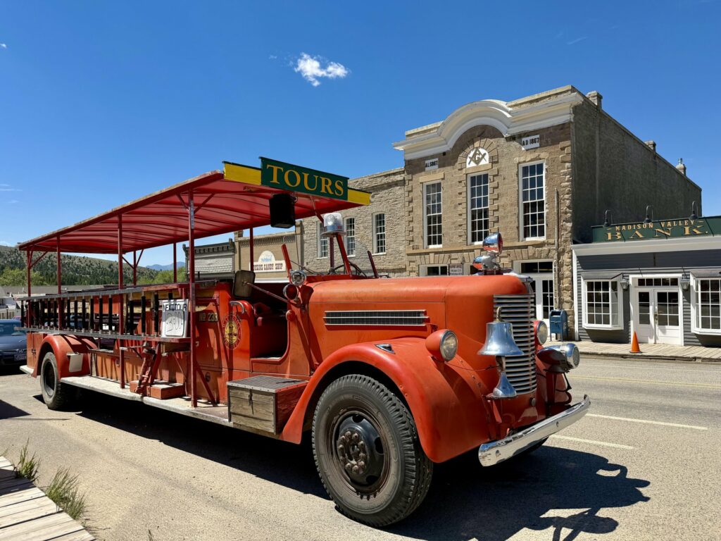 Vintage red fire truck converted for sightseeing tours parked on the main street of Virginia City, Montana, with historic stone buildings including the Madison Valley Bank visible in the background. Photo by Alyssa Starr, Tempest Technologies.