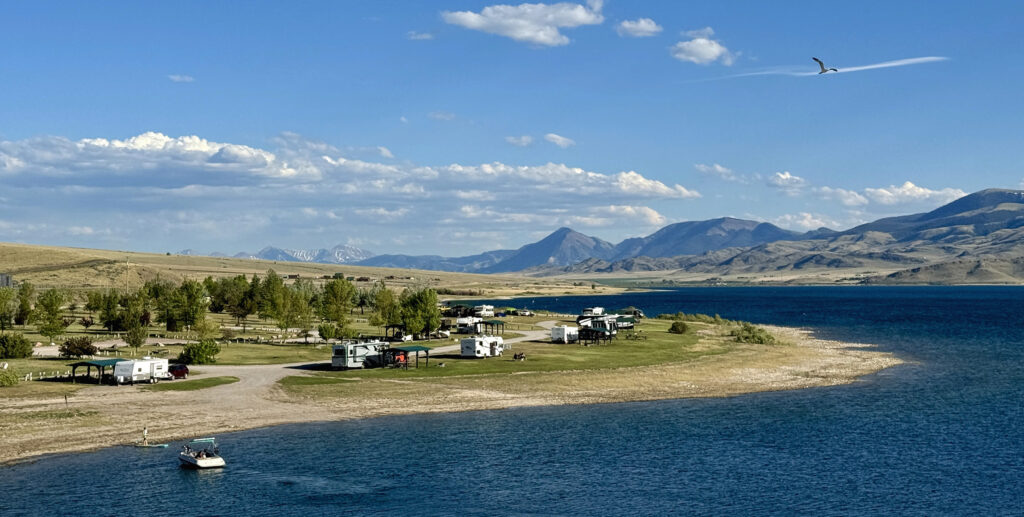 Aerial view of Clark Canyon Reservoir near Dillon, Montana, with an RV campground on a sandy peninsula and a boat heading into shore. The Tendoy Mountains rise in the background. Photo by Rick Graetz.