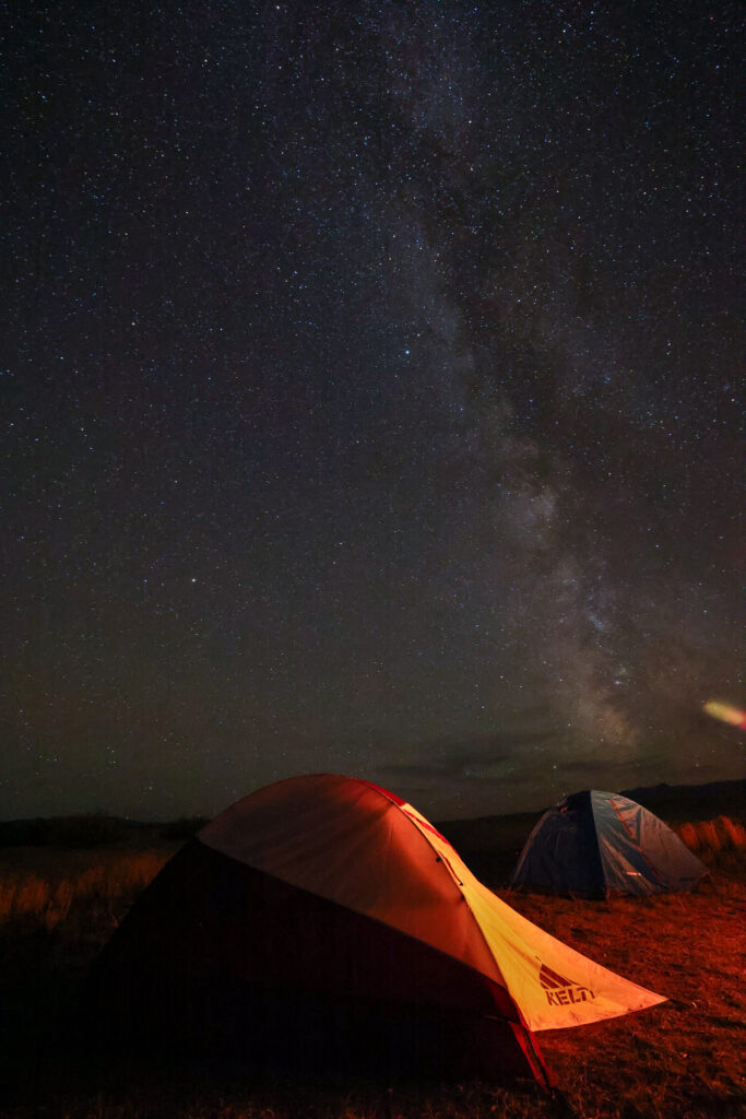 Glowing tents lit from within sit beneath a star-filled night sky at Harrison Lake, Montana, with the Milky Way stretching vividly overhead. The dark, low-light conditions at this Madison County lake make it a prime spot for stargazing and astrophotography. Photo by Sarah Bolt, Tempest Technologies.